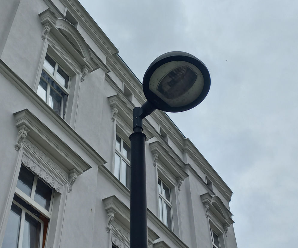 Czarna latarnia uliczna na tle białej kamienicy i zachmurzonego nieba. O inwestycji w Lesznie przeczytasz na Eska Leszno.