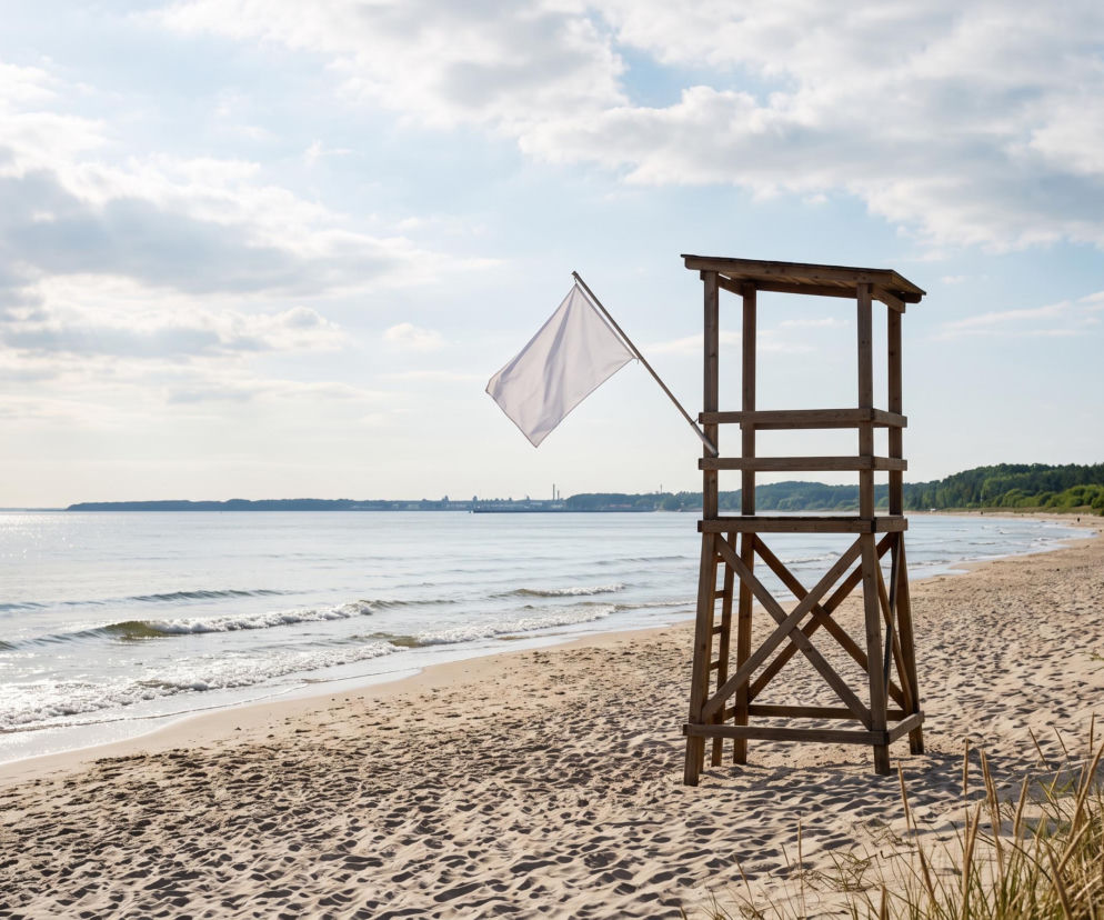 Drewniana wieża ratownicza z białą flagą na pustej plaży w Świnoujściu. O czystości kąpielisk przeczytasz na SE Szczecin.
