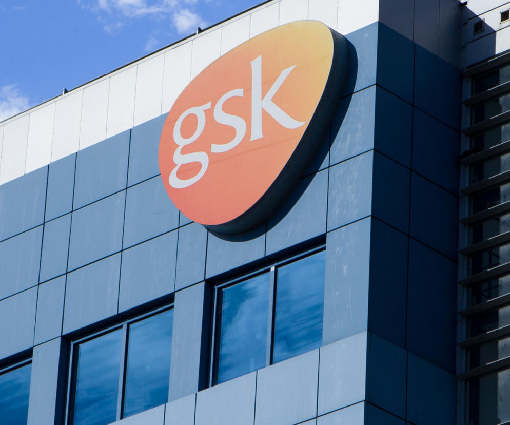 Pomarańczowe logo firmy GSK na elewacji nowoczesnego budynku. O zwolnieniach w Poznaniu przeczytasz na Eska Poznań.