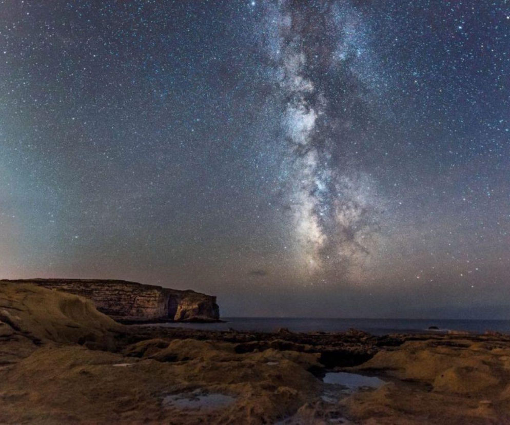 Rozgwieżdżone niebo z Drogą Mleczną nad skalistym brzegiem wyspy Gozo. O trendzie astroturystyki przeczytasz w serwisie Eska.