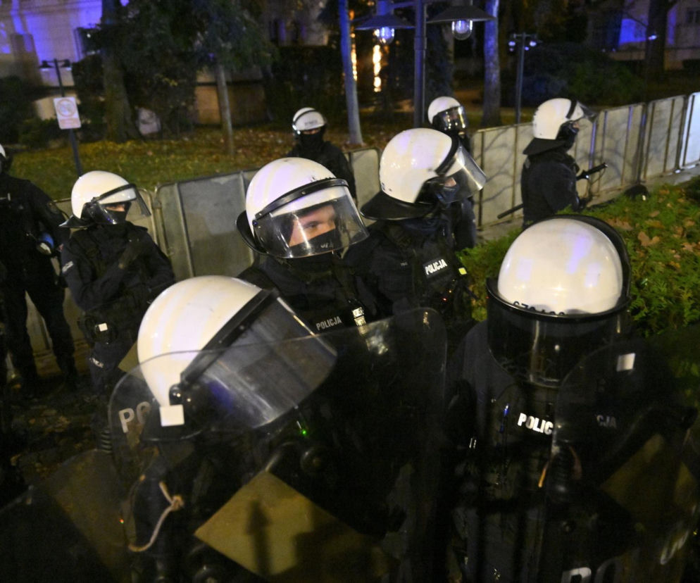 Grupa policjantów w białych kaskach i z tarczami po zmroku. O chaosie pod Trybunałem przeczytasz na SE Polityka.