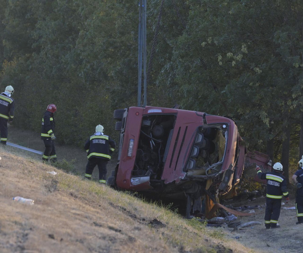 Czerwony autokar leży na boku w przydrożnym rowie. Obok pracują strażacy. O tragedii na Węgrzech przeczytasz na SE.