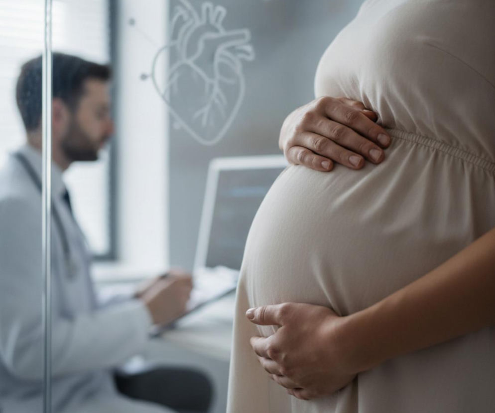 Kobieta w ciąży trzyma dłonie na brzuchu. W tle lekarz. O ryzyku chorób serca u kobiet przeczytasz na Poradnik Zdrowie.