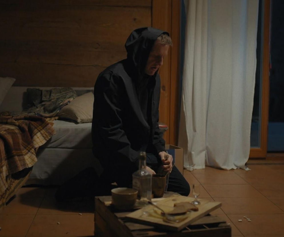 Paweł (Rafał Mroczek) w czarnej bluzie z kapturem klęczy na podłodze, pochylony nad butelką alkoholu i szklanką, rozrzucone obok niej tabletki. Scena ukazuje jego desperację po śmierci Franki w serialu M jak miłość. Więcej informacji o trudnych losach bohaterów na portalu Super Seriale.