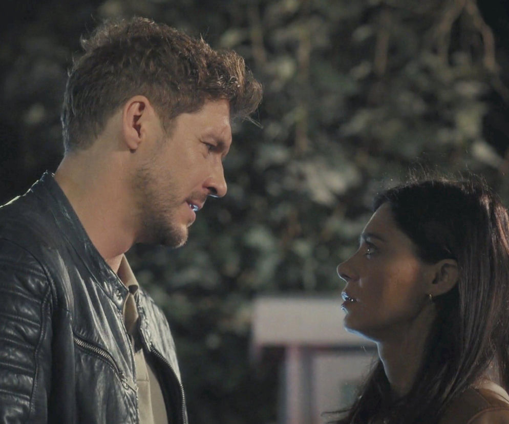 Marcin Chodakowski i Iza Lewińska, bohaterowie serialu M jak miłość, stoją naprzeciwko siebie w scenie nocnej. Marcin (Mikołaj Roznerski) w ciemnej skórzanej kurtce, Iza (Adriana Kalska) w jasnej bluzce, oboje z zaniepokojonymi wyrazami twarzy. Zdjęcie ilustruje kluczowy moment z 1913 odcinka, gdzie Marcin wyznaje Izę, że jest jego rodziną. Więcej o tym na stronie Super Seriale.