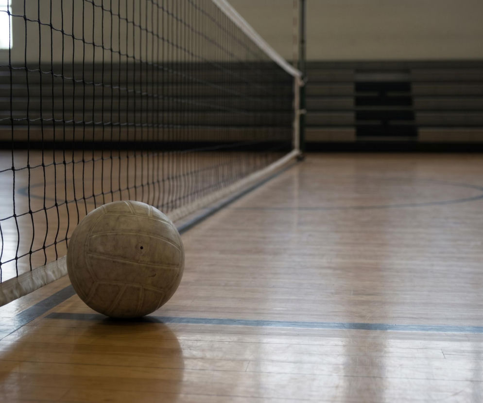 Piłka do siatkówki leżąca przy siatce na drewnianej podłodze hali sportowej, symbolizująca karierę i pasję Daniela Castellaniego. Więcej o trenerze i jego sukcesach przeczytasz na naszym portalu.