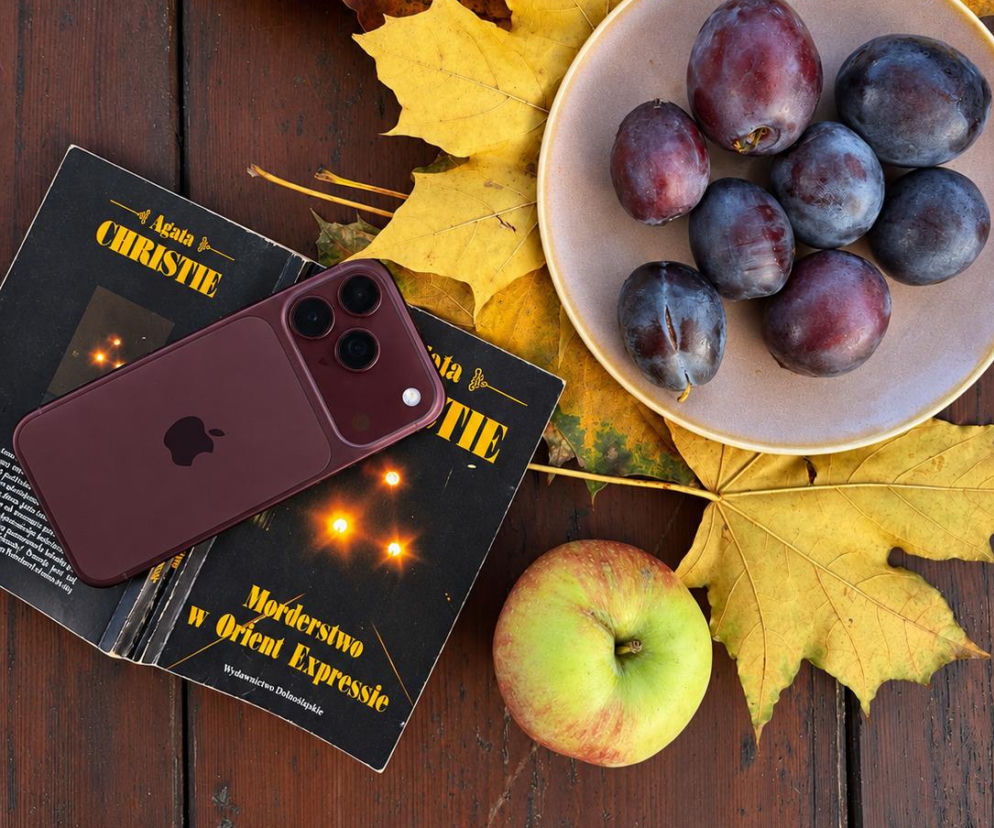 IPhone na książce obok jabłek i śliwek na jesiennych liściach. O testach iPhone'a 18 Pro przeczytasz w Eska.