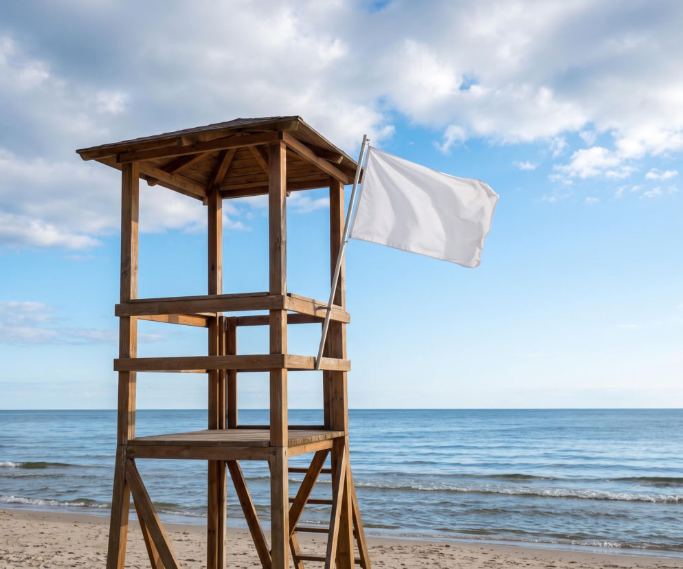 Drewniana wieża ratownicza z białą flagą na plaży w Międzyzdrojach. O bezpieczeństwie nad wodą przeczytasz na SE Szczecin.