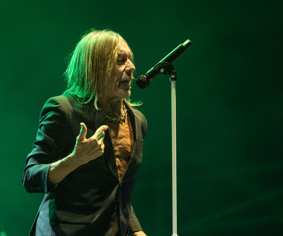 Iggy Pop śpiewa do mikrofonu na scenie w zielonym świetle. O jego współpracy z Mogwai przeczytasz na EskaRock.