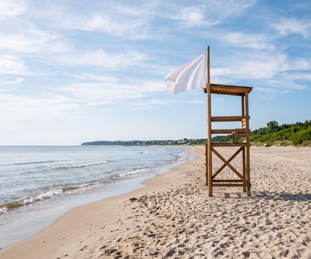 Drewniana wieża ratownicza z białą flagą na plaży w Rewalu. O bezpieczeństwie kąpieli dowiesz się w SE Szczecin.