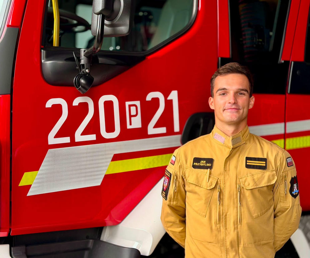 Strażak Jan Przybylski w mundurze na tle czerwonego wozu strażackiego. O jego bohaterskim czynie czytaj w Eska Poznań.