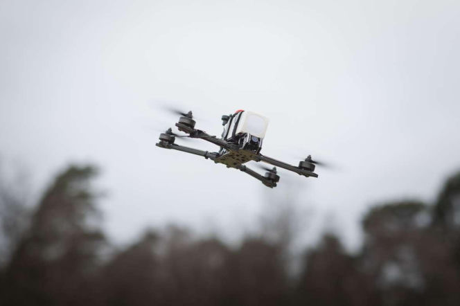Czarny dron z czterema śmigłami leci na tle nieba i drzew. O ochronie przed takimi maszynami pisze SE Portal Obronny.