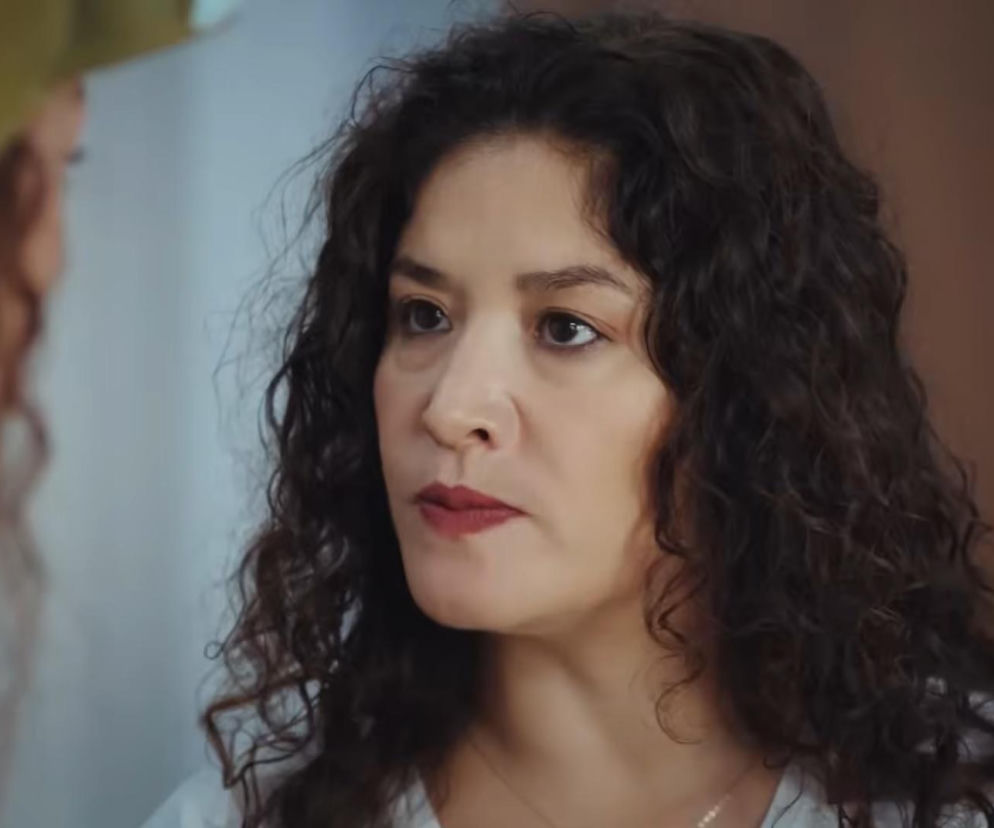 Kobieta z ciemnymi, kręconymi włosami i intensywnym spojrzeniem, przedstawiona w zbliżeniu na twarz. Ma czerwoną szminkę na ustach. Scena ukazuje moment konfrontacji między Cansel a Naną z 877. odcinka Dziedzictwa, o czym przeczytasz na Super Seriale.