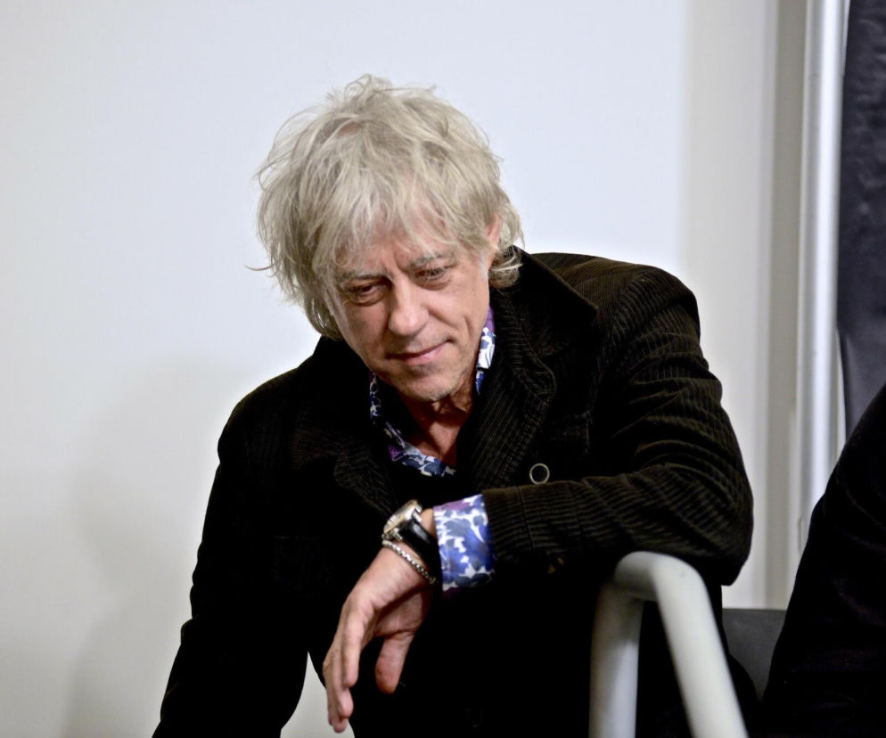 Muzyk Bob Geldof w ciemnej sztruksowej kurtce patrzy w dół. O jego opinii o gwiazdach rocka przeczytasz na EskaRock.