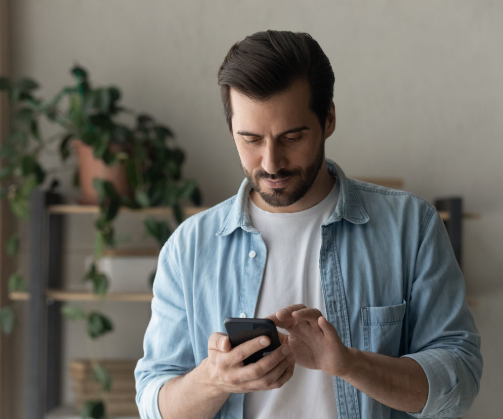 Mężczyzna skupiony na ekranie smartfona. O problemie zdrady online przeczytasz na SE.