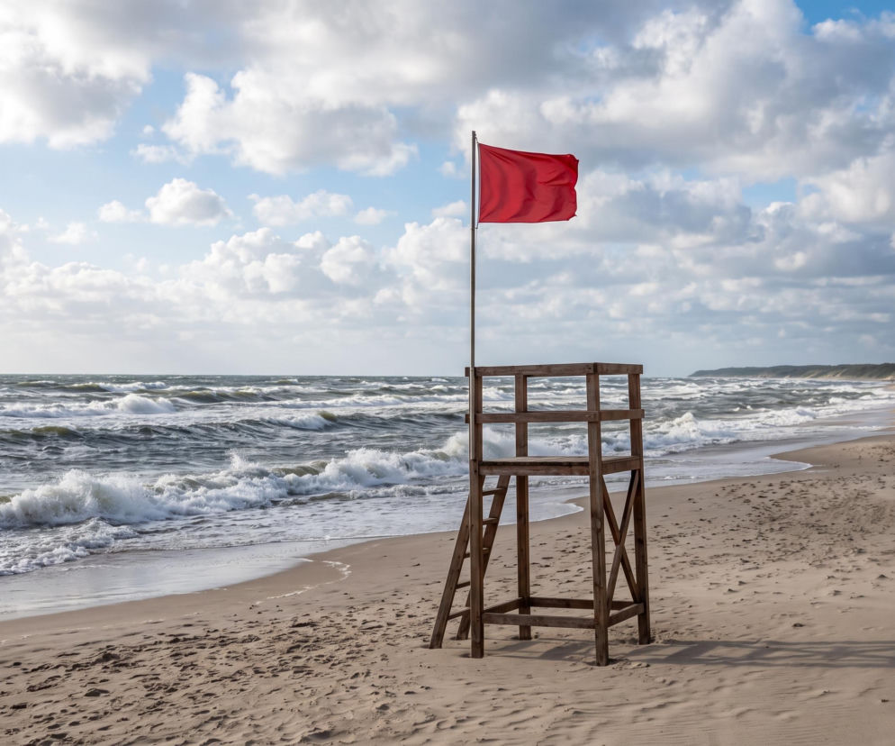 Drewniana wieża ratownicza na plaży z czerwoną flagą zakazującą kąpieli. O pogodzie w Ustroniu Morskim przeczytasz na SE Szczecin.