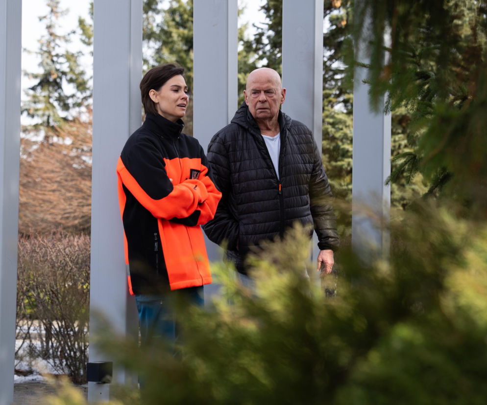 Pola Gonciarz (Blanka) w czarno-pomarańczowej kurtce i Piotr Garlicki (Tretter) w czarnej puchówce, stojący na zewnątrz z zmartwionymi minami. Ujęcie od pasa w górę, w tle drzewa i elementy architektury. Zdjęcie ilustruje odcinek serialu Na dobre i na złe, o którym przeczytasz na Super Seriale.