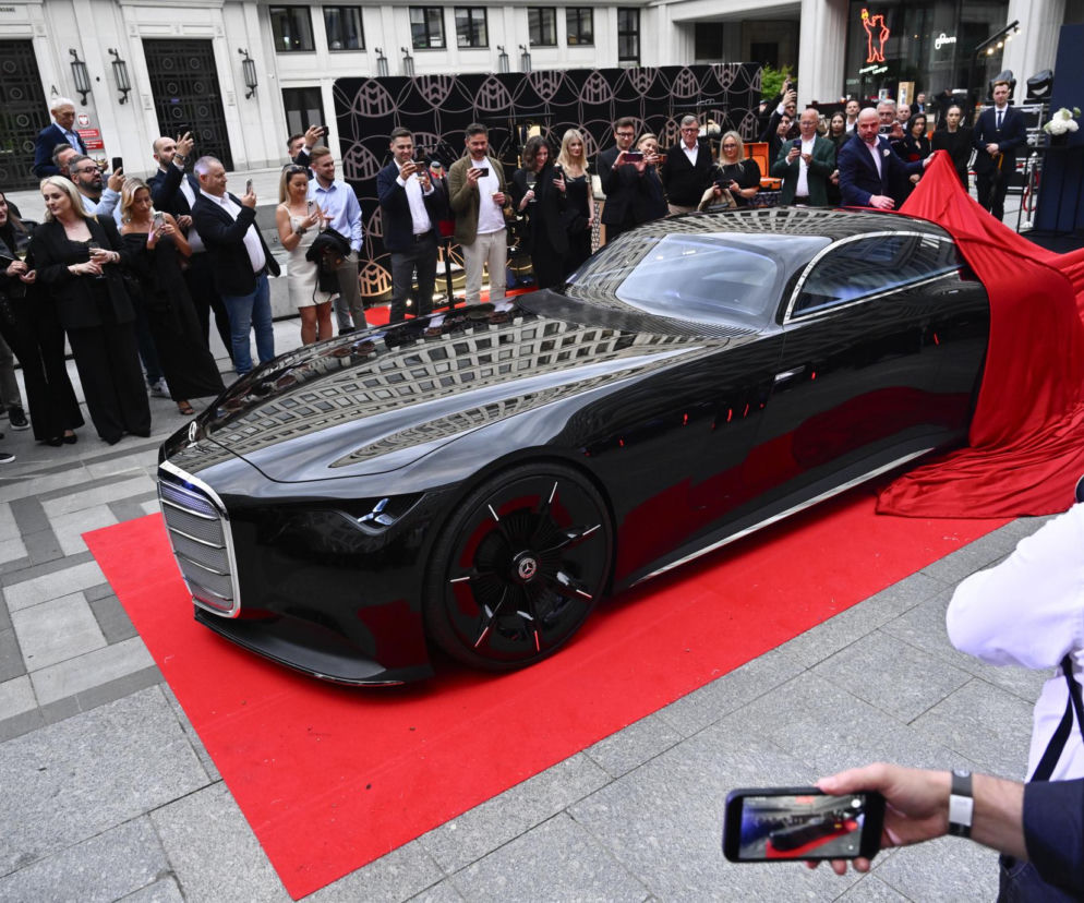 Odsłonięcie czarnego, luksusowego samochodu Mercedes Vision Iconic na czerwonym dywanie przed budynkiem w centrum Warszawy podczas otwarcia Maybach Atelier. Wydarzenie przyciągnęło wielu gości, dokumentujących moment zdjęciami, o czym więcej przeczytasz na naszym portalu.