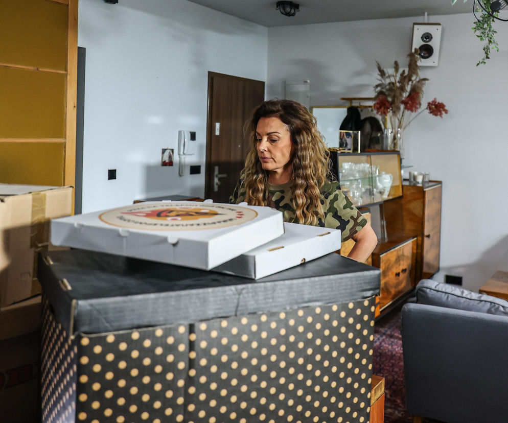 Kobieta stojąca przy stercie pudeł i pudełkach z pizzą. O serialu Szpital św. Anny przeczytasz na Eska.
