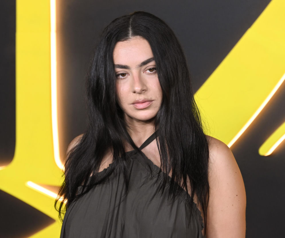 Piosenkarka Charli XCX z długimi, ciemnymi włosami na tle żółtych pasów. O jej muzycznych rekordach przeczytasz w Eska.