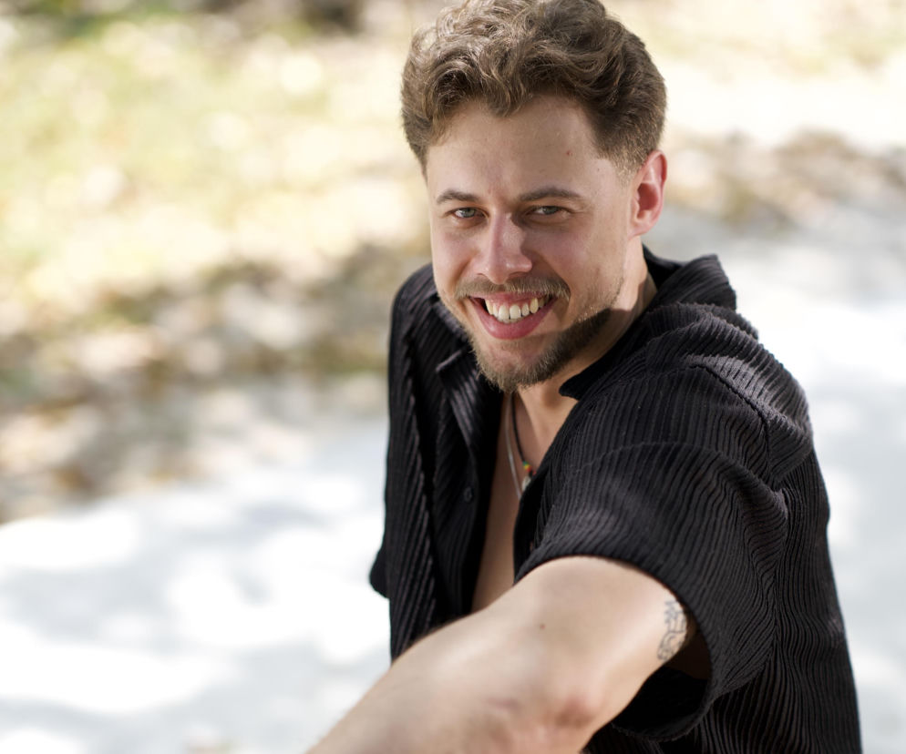Uśmiechnięty Wiktor Borzych z Hotelu Paradise 13 siedzi na kamieniu. O nowym uczestniku show przeczytasz na Eska2.