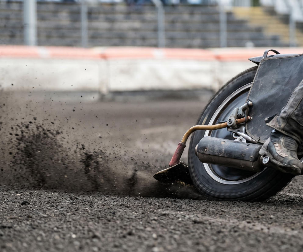 Żużlowiec w czarnym kombinezonie pędzi na motocyklu po torze żużlowym, unosząc tumany ziemi. Dynamiczne ujęcie ukazuje moc i prędkość podczas zawodów żużlowych, o których więcej przeczytasz na naszym portalu.