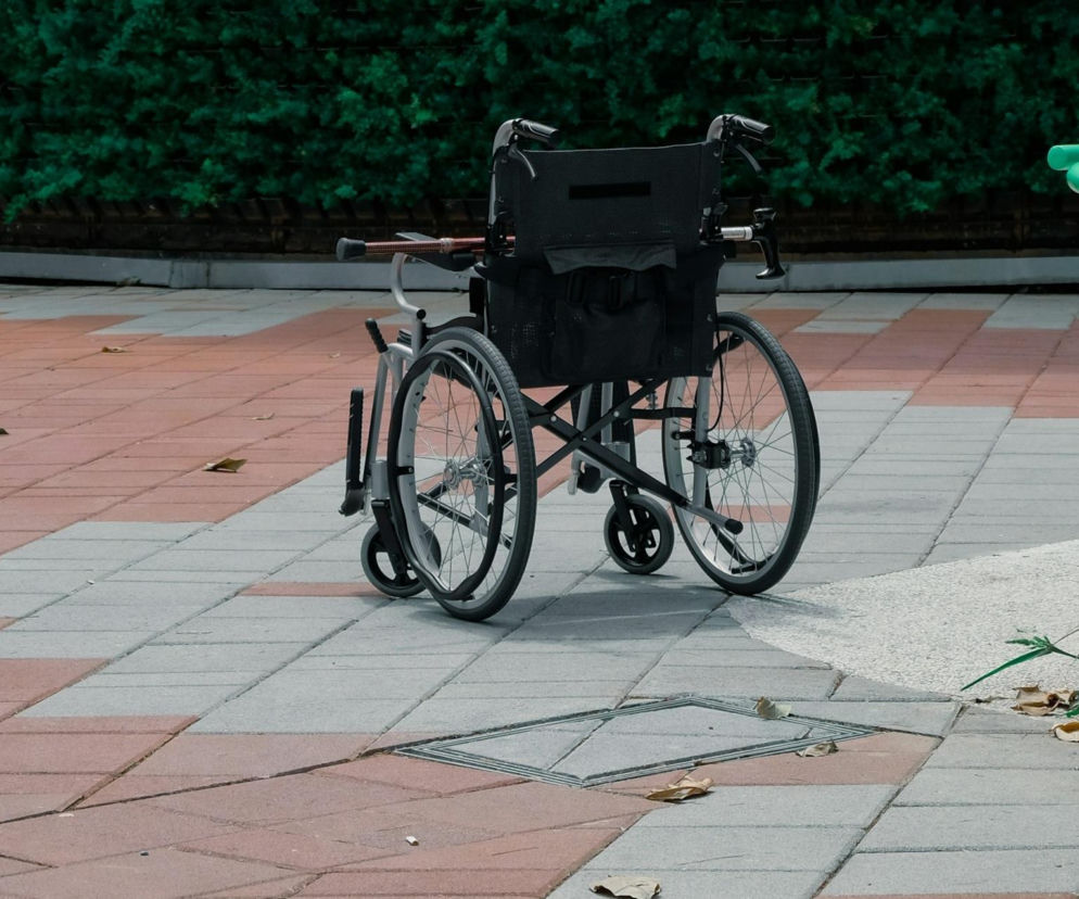Pusty wózek inwalidzki stoi na chodniku z kostki brukowej. O tragicznej śmierci seniorki w Żarowie przeczytasz na SE Wrocław.