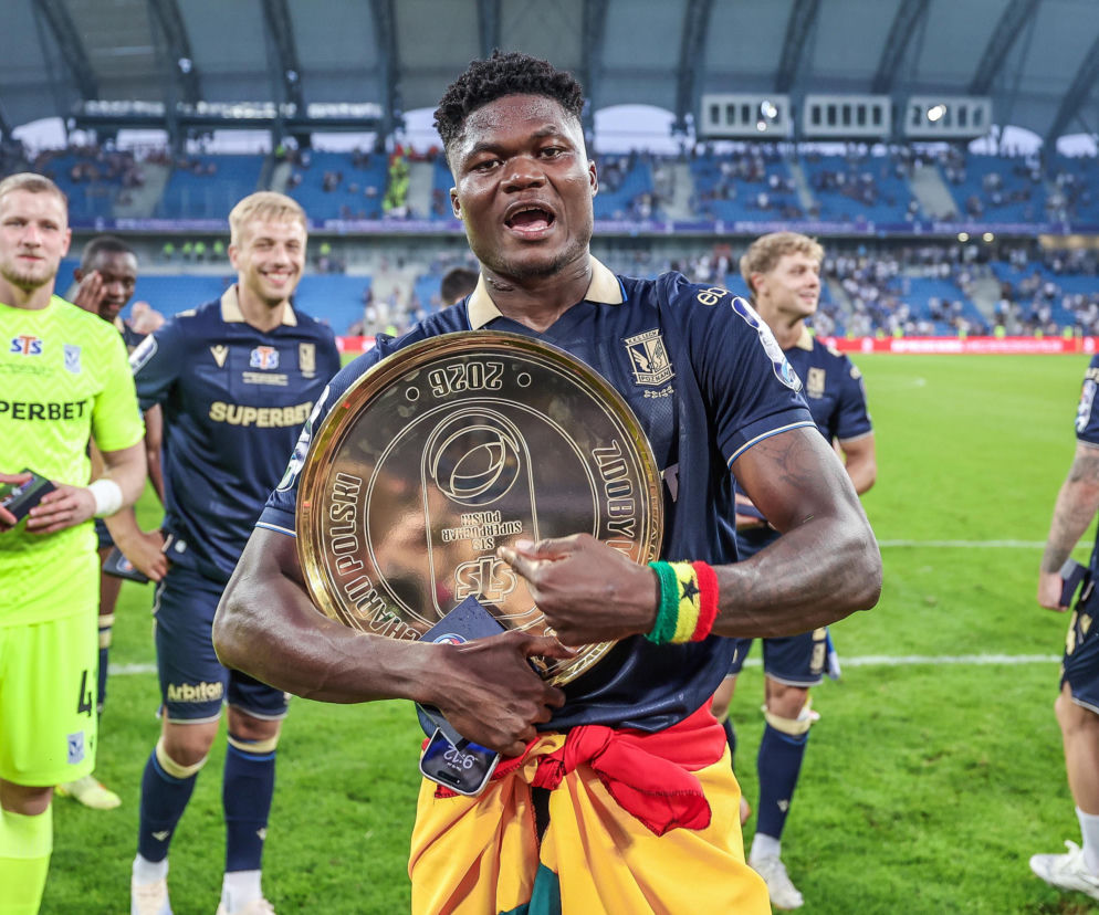 Obrońca Terry Yegbe trzyma trofeum na murawie stadionu. O sukcesach piłkarza Lecha Poznań przeczytasz na SE Supersport.