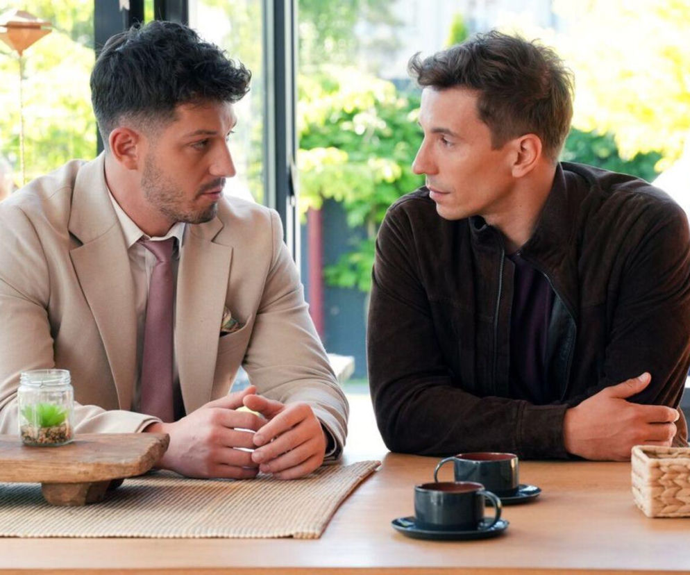 Justin (Jasper Sołtysiewicz) w beżowym garniturze i Tomasz (Jakub Sokołowski) w brązowej kurtce siedzą przy stole i rozmawiają. Ich strategiczne plany dotyczące przejęcia hotelu Stańskiego to kluczowy wątek w Barwach szczęścia, o którym przeczytasz na portalu Super Seriale.