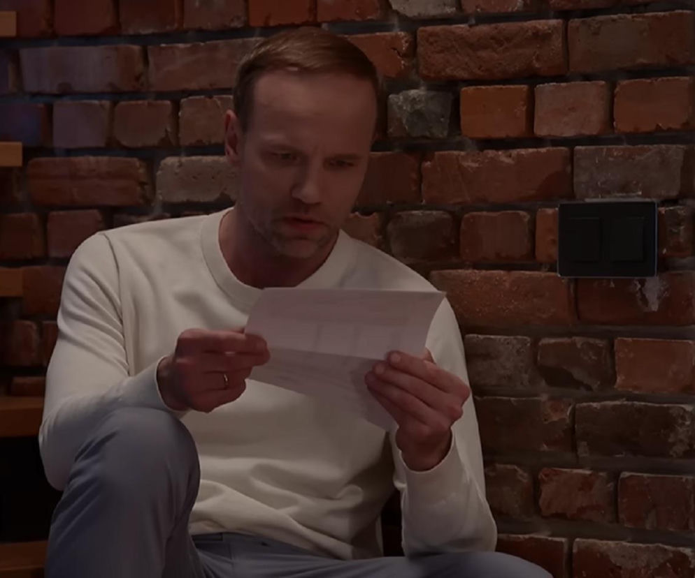 Janek (Maciej Mikołajczyk) z serialu Pierwsza miłość czyta z niedowierzaniem wyniki testu DNA w swoim mieszkaniu z ceglaną ścianą w tle. Mężczyzna trzyma w dłoniach kartkę z informacjami o ojcostwie Poli. Więcej o losach bohatera przeczytasz na Super Seriale.