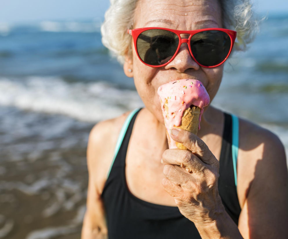 Seniorka w czerwonych okularach je loda na plaży. O rekordowej liczbie stulatków w Japonii przeczytasz w Eska.
