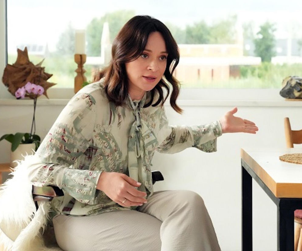 Maria Dejmek jako Natalia Zwoleńska z serialu Barwy szczęścia, siedząca przy stole i gestykulująca. Jest wyraźnie wzburzona rozmową z Cezarym. Ten fragment z Barw szczęścia i inne informacje znajdziesz na portalu Super Seriale.