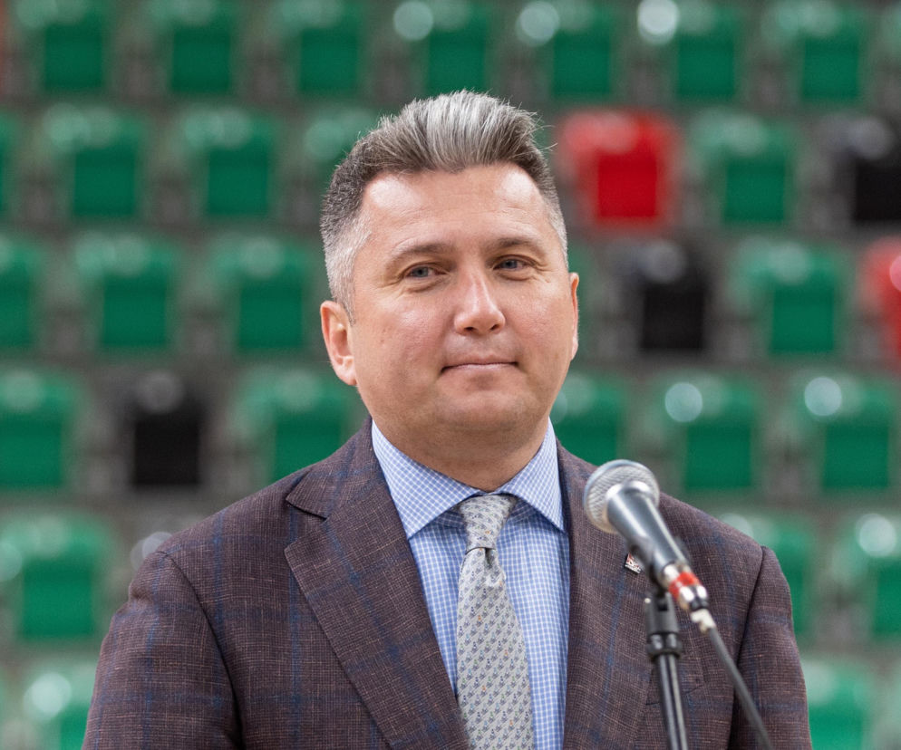 Prezes PKOl Radosław Piesiewicz stoi przy mikrofonie na tle trybun. O jego zatrzymaniu przeczytasz na SE Polityka.