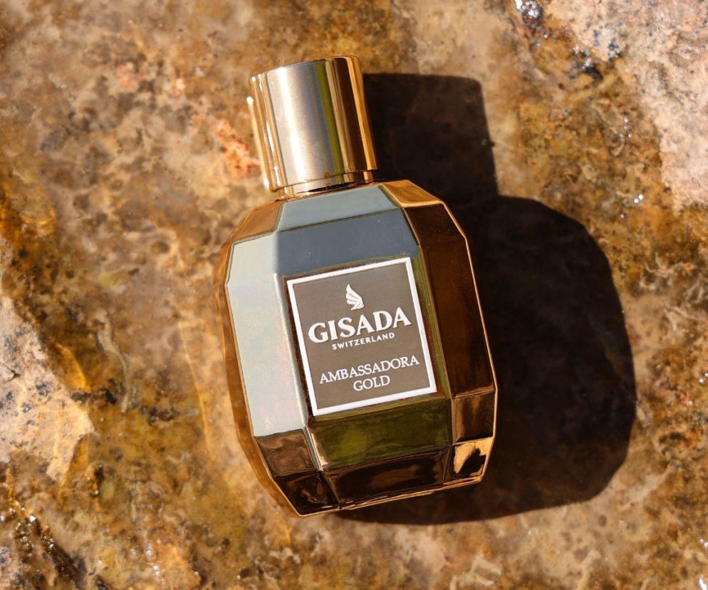 Złoty flakon perfum Gisada Ambassadora Gold na kamiennym tle z wodą. O zapachowym alter ego przeczytasz na Eska.