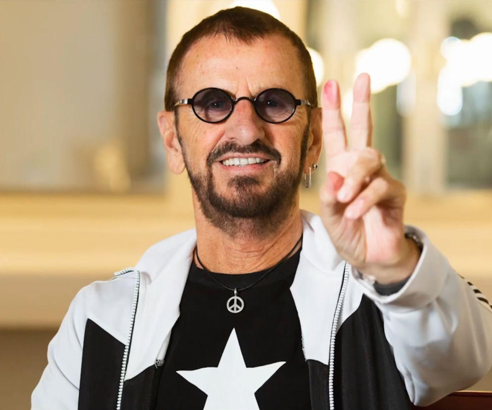 Uśmiechnięty Ringo Starr pokazuje palcami znak pokoju. O radach perkusisty The Beatles przeczytasz na EskaRock.