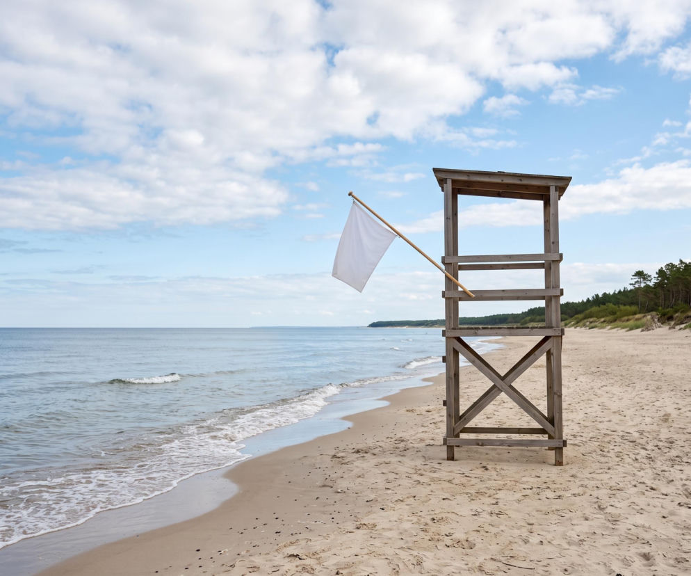 Drewniana wieża ratownicza z białą flagą na pustej plaży w Pogorzelicy. O warunkach nad morzem przeczytasz na SE Szczecin.