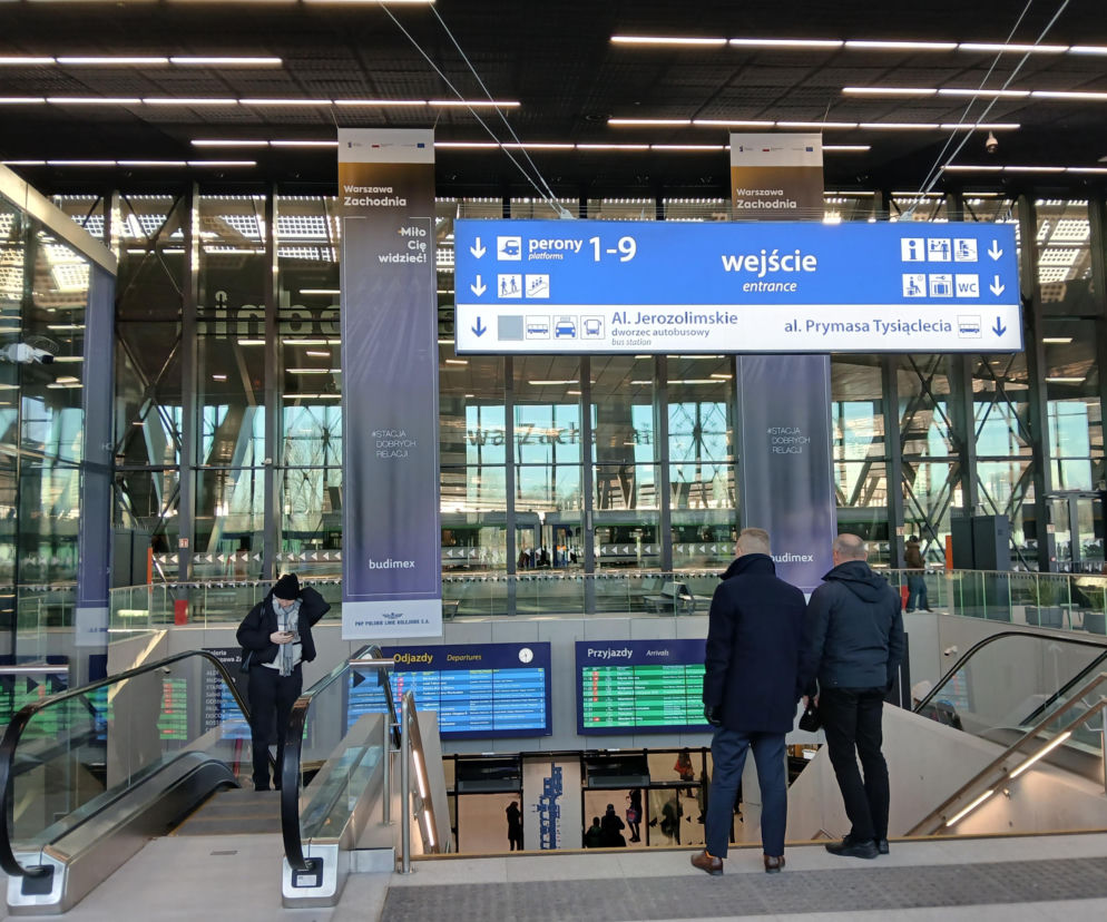 Wnętrze Dworca Warszawa Zachodnia w trakcie modernizacji, z widocznymi ruchomymi schodami, tablicami odjazdów i przyjazdów oraz informacjami o peronach i wyjściach. Przebudowa dworca pokazuje, jak istotne są inwestycje w kolej, o których czytasz na Super Biznes.