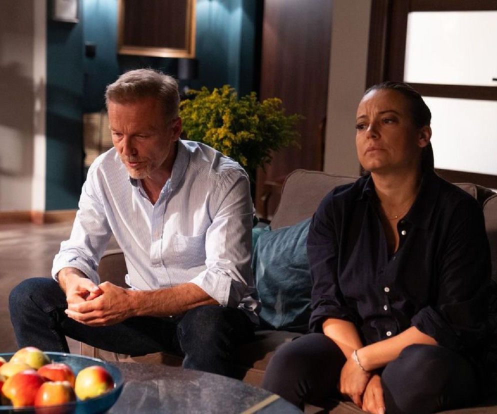 Magda i Andrzej Budzyńscy siedzą na kanapie w domu, Magda jest zmartwiona po wyjściu z aresztu, a Andrzej wspiera żonę. Scena z serialu M jak miłość w 1898 odcinku. Więcej o ich losach na stronie Super Seriale.