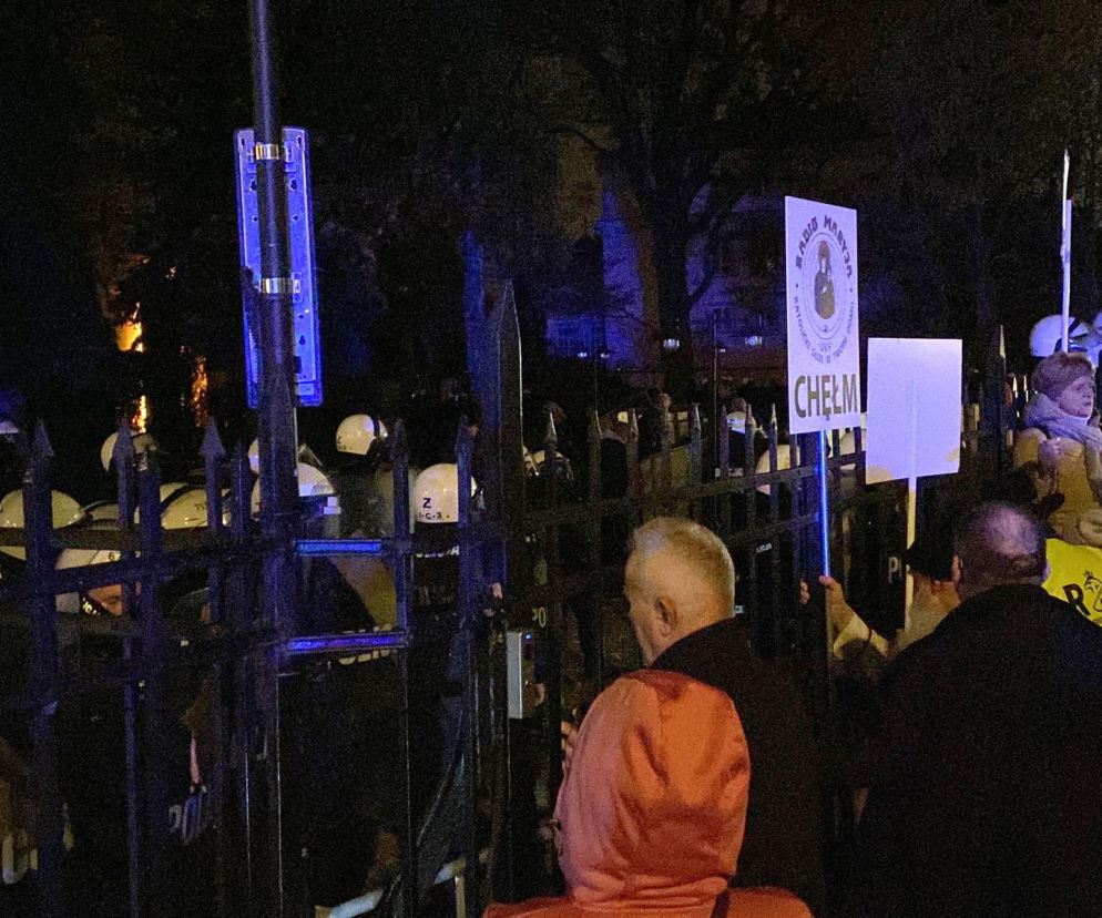 Ludzie stoją przed bramą Trybunału Konstytucyjnego w nocy. O interwencji policji przeczytasz na SE Polityka.