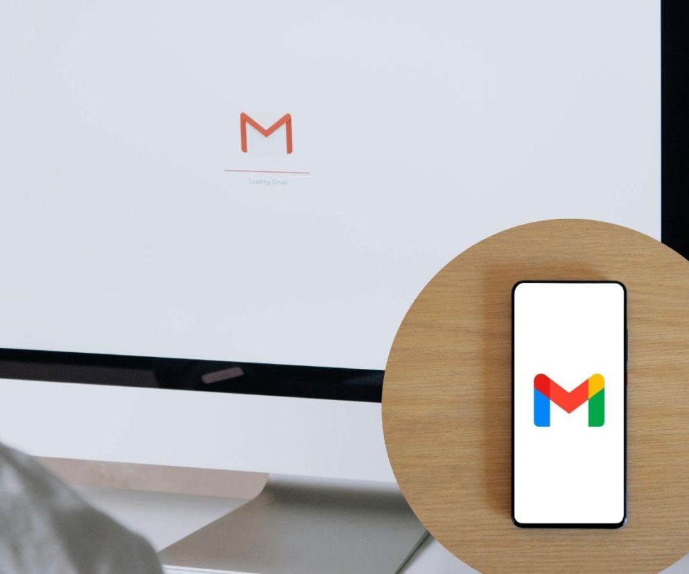 Logo Gmaila widoczne na ekranie komputera z napisem Loading Gmail oraz na smartfonie na drewnianym blacie. Obraz symbolizuje nową funkcję AI w Gmailu i jest kontekstualnie związany z treścią, o której można przeczytać na Super Biznes.