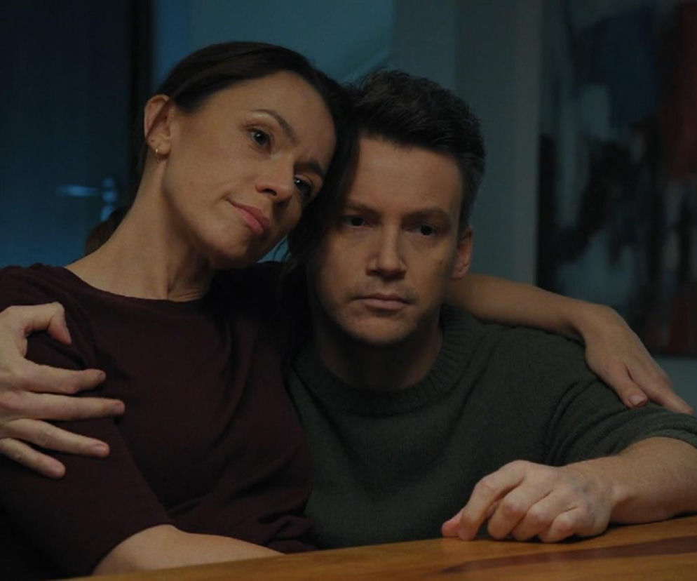 Aktorka Magdalena Turczeniewicz jako Martyna i aktor Mikołaj Roznerski jako Marcin, przytuleni siedzą przy stole. Martyna opiera głowę na ramieniu Marcina, wyrażając poczucie ulgi i pożegnania z dawną miłością, co jest kluczowe dla fabuły serialu M jak miłość. Więcej o tym na Super Seriale.