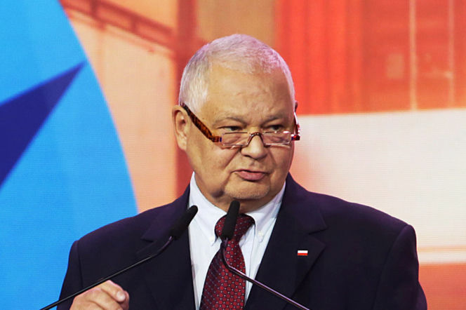 Adam Glapiński, prezes NBP, w okularach i garniturze, z dwoma mikrofonami przed sobą, podczas konferencji dotyczącej finansowania zbrojeniówki, o czym można przeczytać na Super Biznes.