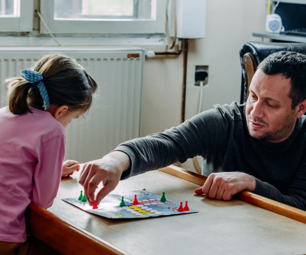Ojciec grający z córką w grę planszową. O tym, jak pomóc dziecku opanować złość po przegranej, przeczytasz na SE.