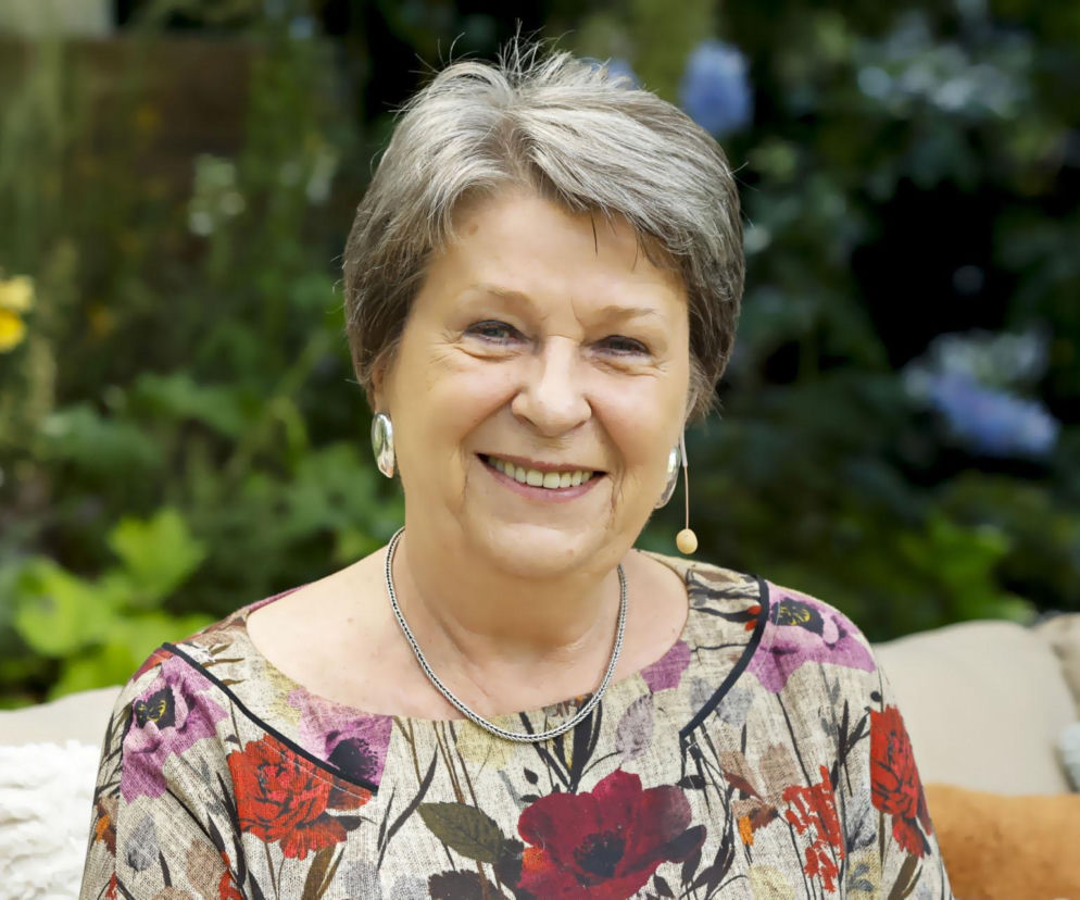 Dr Irena Eris uśmiecha się na tle zielonej roślinności, ubrana w kwiecistą bluzkę i srebrny naszyjnik. Założycielka kosmetycznego imperium opowiada o kulisach biznesu bez komórki na portalu Super Biznes.