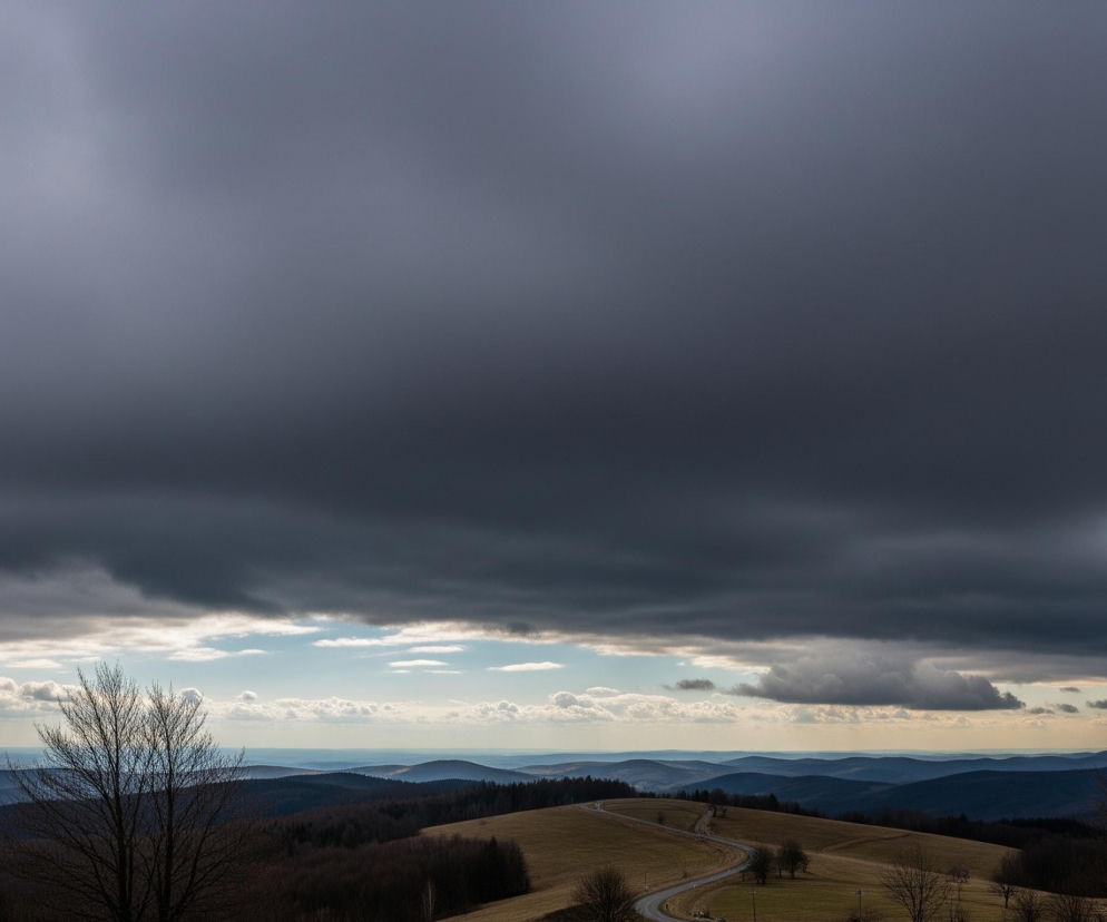 Dominującym elementem jest rozległe, ciemnoszare zachmurzone niebo, zajmujące większą część górnej połowy obrazu, z jaśniejszymi fragmentami na lewej górze. Poniżej rozciąga się pofałdowany krajobraz górski, z licznymi pasmami wzniesień o różnych odcieniach błękitu i zieleni, zanikających w oddali. Na środkowym planie wijąca się droga asfaltowa przecina brązowo-zielone pola, prowadząc w głąb obrazu. Z lewej i prawej strony kadru, na pierwszym planie, widoczne są fragmenty nagich drzew.
