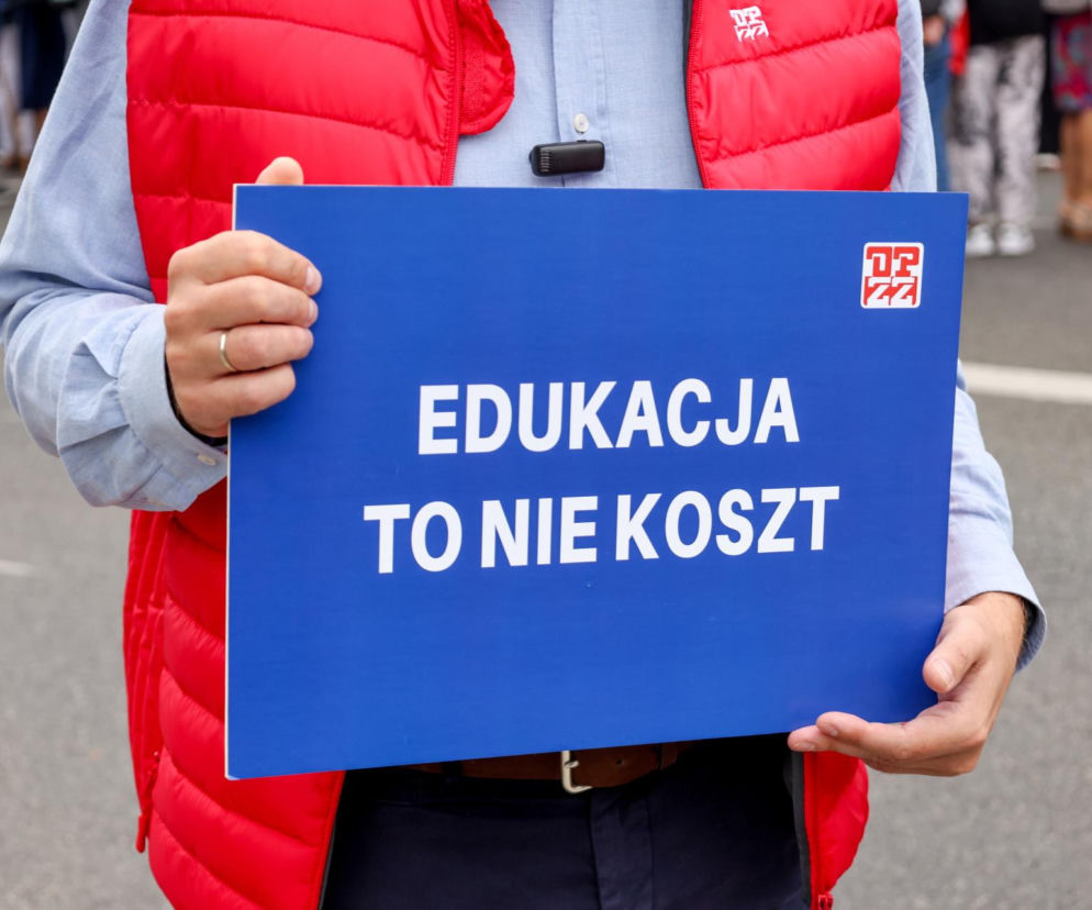 Osoba w czerwonej kamizelce trzyma tablicę z napisem Edukacja to nie koszt. O protestach ZNP przeczytasz w Eskalo.
