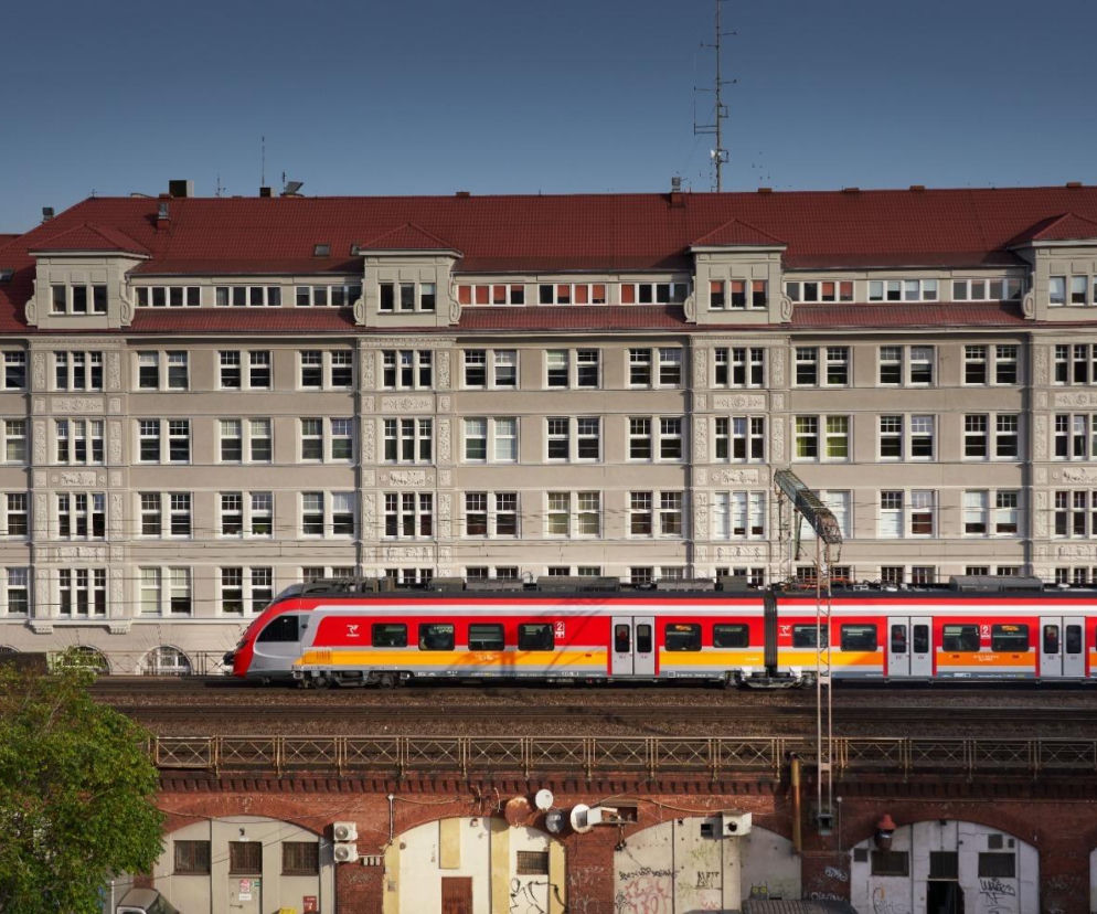 Czerwono-żółty pociąg Polregio na tle kamienicy. O zasadach podróży z psem i kotem przeczytasz na SE.