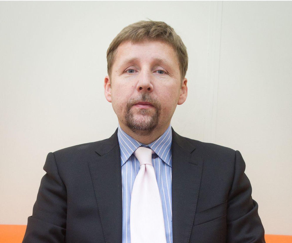 Marek Migalski, były europoseł i profesor, patrzy prosto w obiektyw. Ma ciemną marynarkę, błękitną koszulę w paski i jasnoróżowy krawat. Apeluje o profilaktykę nowotworową, o czym możesz przeczytać więcej na Poradnik Zdrowie.