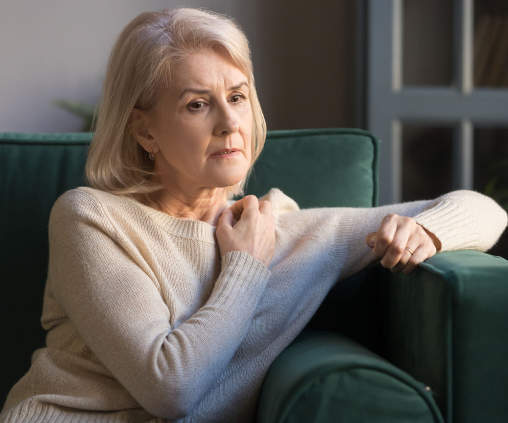 Zasmucona dojrzała kobieta siedzi na zielonej kanapie. O psychicznych objawach menopauzy przeczytasz na Poradnik Zdrowie.