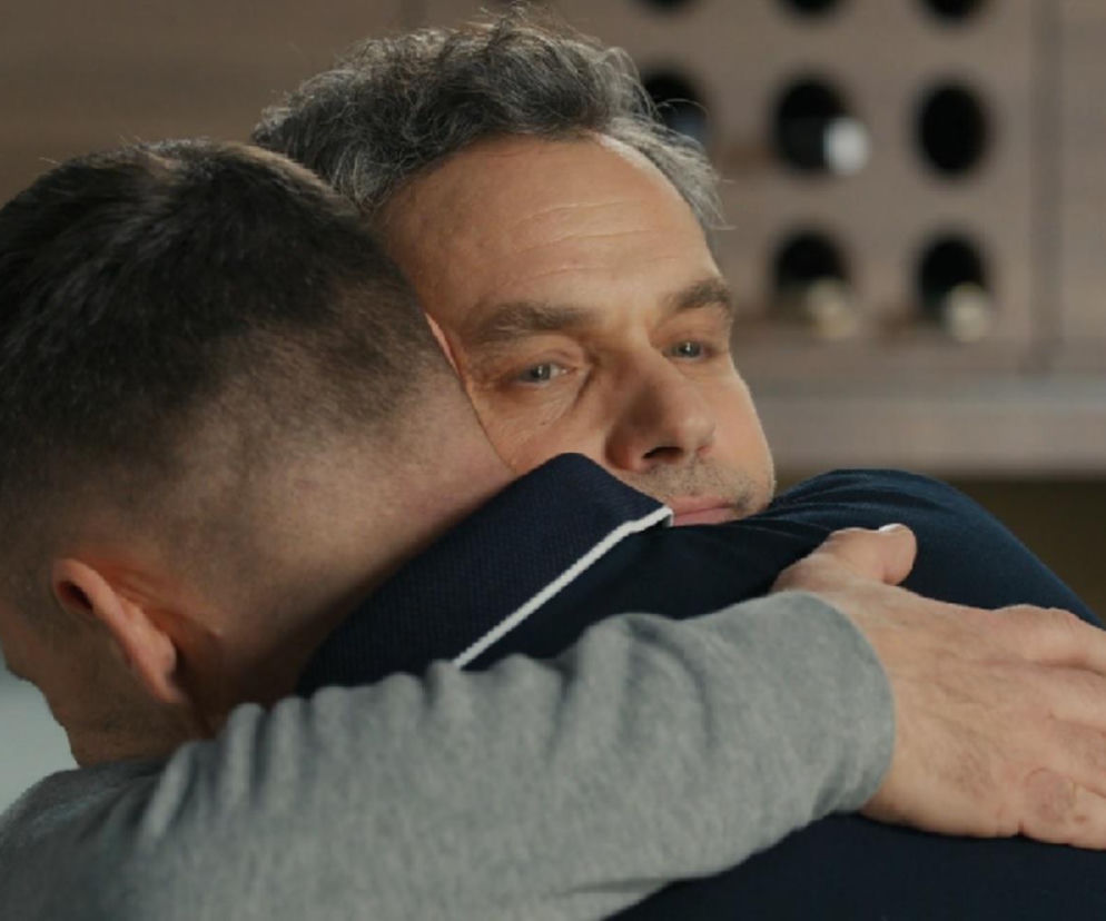 Dwóch mężczyzn, Darek (Andrzej Niemyt) i Karol (Jan Wieczorkowski) z serialu Barwy szczęścia, w czułym uścisku, symbolizującym ich związek i wspólną rocznicę. Karol opiera głowę na ramieniu Darka. Emocje związane z tragicznym finałem ich rocznicy. Więcej o tym na Super Seriale.